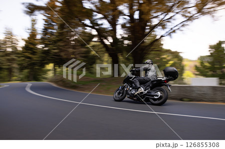 Driver riding motorcycle on empty asphalt road, spring mountains 126855308