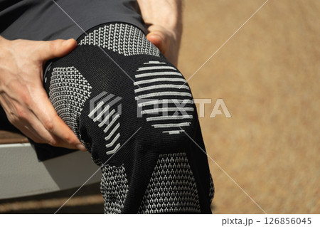 Man putting knee brace to support painful leg. Athlete bodybuilder leg wearing knee support brace or elastic kneecap bandage. Sleeve for compression. Health problems and pain. Man putting knee brace to support painful leg. Athlete bodybuilder leg wearing knee support brace or elastic kneecap bandage. Sleeve for compression. Health problems and pain. 126856045