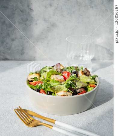 Salad with lettuce, tomatoes, croutons, olives and parmesan cheese in a bowl on a light background Salad with lettuce, tomatoes, croutons, olives and parmesan cheese in a bowl on a light background 126856267