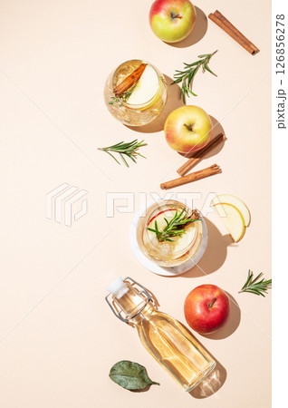 Flat lay of apple cocktail or cider in a glass with ice, cinnamon and rosemary, bottle and fruits 126856278