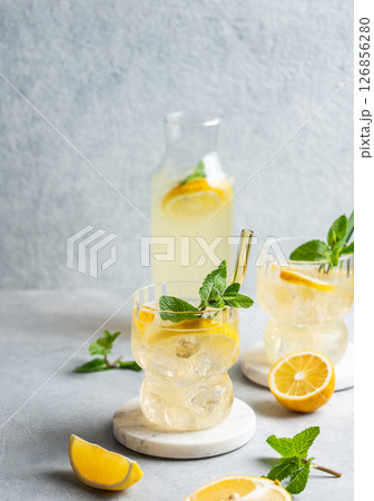 Two glasses of fresh drink lemonade with lemon, mint and ice on a light background with bottle Two glasses of fresh drink lemonade with lemon, mint and ice on a light background with bottle 126856280