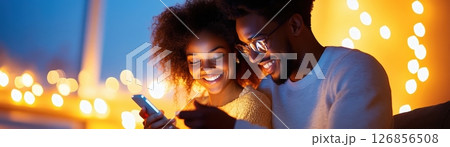 Affectionate African American couple embracing and enjoying a romantic date night out on the city street surrounded by twinkling holiday lights and a festive atmosphere  They are smiling 126856508