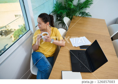 Woman Reflecting by Window During Coffee Break in Cozy Workspace Woman Reflecting by Window During Coffee Break in Cozy Workspace 126857083