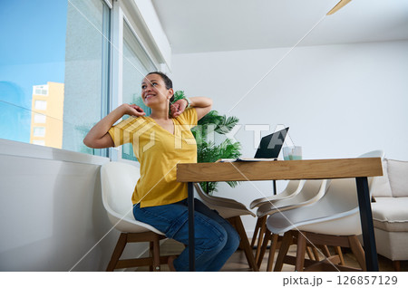 Smiling Woman Stretching in Home Office with Laptop During Work Break 126857129