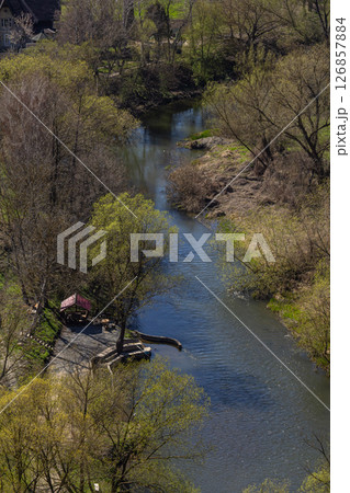 Calm river flowing through a natural landscape with trees and a small dock on a sunny spring day 126857884