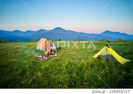 Scenic mountain campsite with two tents in morning. Two campers enjoying serene view of rolling mountains under clear sky. Picturesque sunrise landscape, creating tranquil and cozy outdoor experience. Scenic mountain campsite with two tents in morning. Two campers enjoying serene view of rolling mountains under clear sky. Picturesque sunrise landscape, creating tranquil and cozy outdoor experience. 126858157