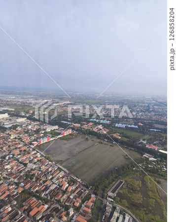 Aerial view of a suburban residential area surrounded by green fields and urban development under a cloudy sky. 126858204