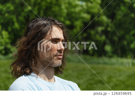 Portrait of thoughtful handsome caucasian brunette man with long curly hair enjoying nature and looking away. Summer vacation. Slow living. 126859695