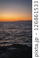 Rocky coastline meeting calm ocean under a vibrant sunset sky 126861533