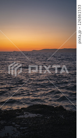 Rocky coastline meeting calm ocean under a vibrant sunset sky 126861533