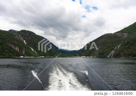 Fjord village and twin waterfalls seen from catamaran wake near Bergen, Norway 126861600