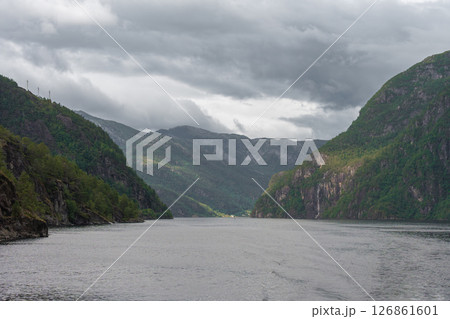 Dramatic fjord landscape with cloudy sky and distant village in Norway Dramatic fjord landscape with cloudy sky and distant village in Norway 126861601