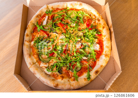 Fresh vegetable pizza with arugula in cardboard box on wooden table, sunlight, selective focus Fresh vegetable pizza with arugula in cardboard box on wooden table, sunlight, selective focus 126861606
