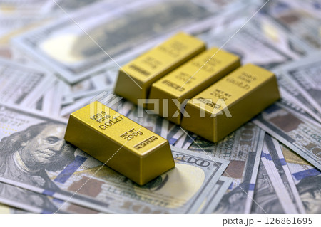 Gold bars rest on background of dollar bills, symbolizing wealth and financial investment. image conveys sense of prosperity and economic stability Gold bars rest on background of dollar bills, symbolizing wealth and financial investment. image conveys sense of prosperity and economic stability 126861695