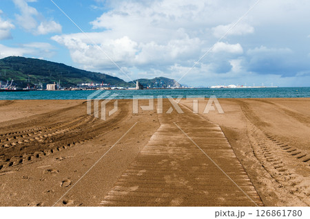A wooden pathway and tire tracks lead towards the sea on a tranquil, cloudy beach. Getxo, Bilbao 126861780