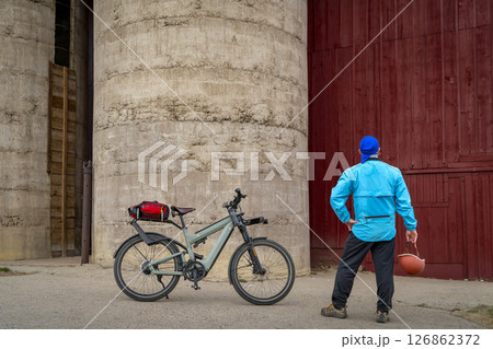 senior male cyclist with a touring electric bike is taking a rest break at old barn in rural Colorado 126862372
