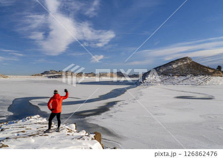 male hiker in down jacket on a rocky shore of frozen Horsetooth Reservoir in northern Colorado 126862476