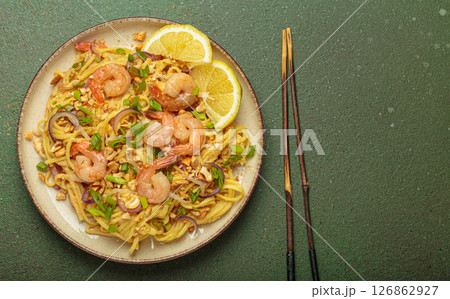 Pad thai noodles with shrimps and chopsticks on rustic green background, traditional dish of Thailand, space for text Pad thai noodles with shrimps and chopsticks on rustic green background, traditional dish of Thailand, space for text 126862927
