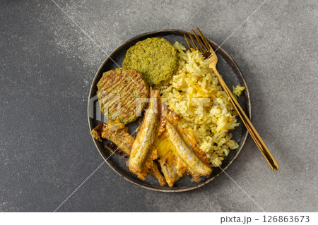 A wholesome breakfast featuring turmeric rice with baked ocean fish, complemented by broccoli pancakes and roasted vegetables, offering a nutritious and satisfying meal A wholesome breakfast featuring turmeric rice with baked ocean fish, complemented by broccoli pancakes and roasted vegetables, offering a nutritious and satisfying meal 126863673