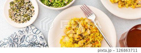 Stewed rice with chicken breast and mixed salad with radishes and various seeds, a served table with food and a vase of flowers 126863711