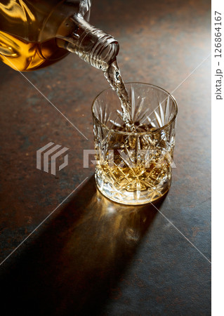 Whisky pour from a bottle into a cut glass tumbler. 126864167