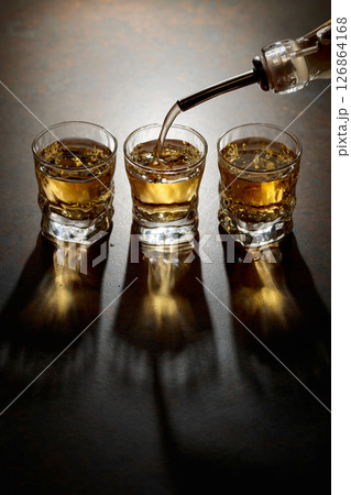 Whiskey pour from a bottle into a small glasses. 126864168