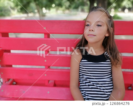 The girl sits on a bench in park. There is a flower ornament on her head. High quality photo 126864276