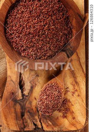 Natural red rice, in a wooden bowl and spoon on a wooden surface in rustic style, top view 126864310