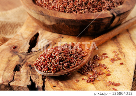 Natural red rice, in a wooden bowl and spoon on a wooden surface in rustic style, top view 126864312