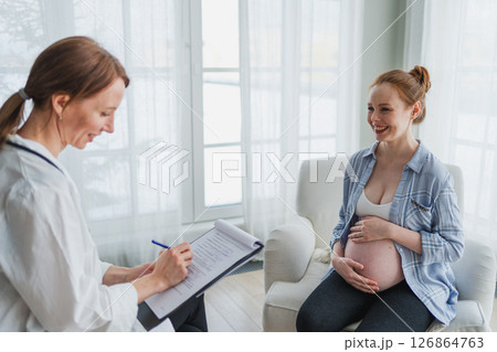Female doctor examining pregnant woman in doctor office. Pregnant girl patient have consultation in hospital. Gynecologist doctor consulting patient about pregnancy. Visit to doctor medical checkup Female doctor examining pregnant woman in doctor office. Pregnant girl patient have consultation in hospital. Gynecologist doctor consulting patient about pregnancy. Visit to doctor medical checkup 126864763