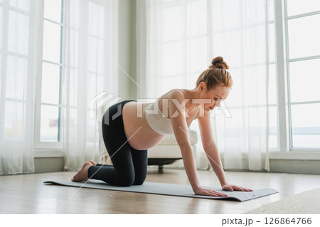 Pregnancy yoga fitness workout training. Pregnant woman practicing yoga at home. Pregnant girl doing sports exercise on yoga mat indoor. Woman with big belly have fitness training practicing asana 126864766