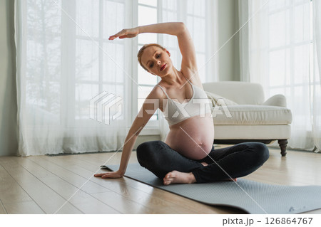 Pregnancy yoga fitness workout training. Pregnant woman practicing yoga at home. Pregnant girl doing sports exercise on yoga mat indoor. Woman with big belly have fitness training practicing asana Pregnancy yoga fitness workout training. Pregnant woman practicing yoga at home. Pregnant girl doing sports exercise on yoga mat indoor. Woman with big belly have fitness training practicing asana 126864767