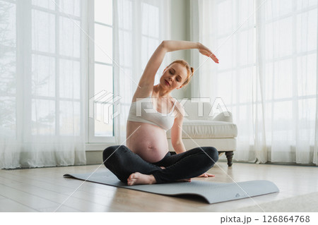 Pregnancy yoga fitness workout training. Pregnant woman practicing yoga at home. Pregnant girl doing sports exercise on yoga mat indoor. Woman with big belly have fitness training practicing asana 126864768