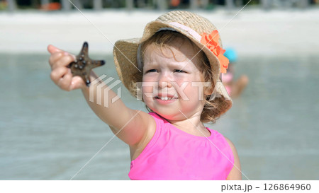 Baby girl holds starfish while relaxing on tropical beach with family Baby girl holds starfish while relaxing on tropical beach with family 126864960