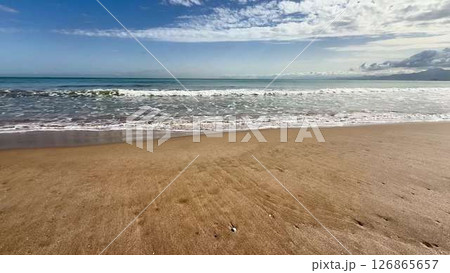 Enjoy a serene beach view showcasing rolling waves, a vibrant blue sky, and tranquility 126865657