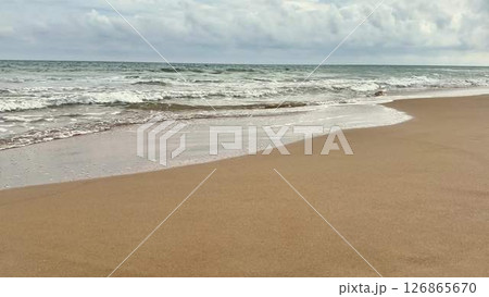 A Serene Beach Scene Featuring Gentle Ocean Waves, Fluffy Clouds, and Calm Skies 126865670