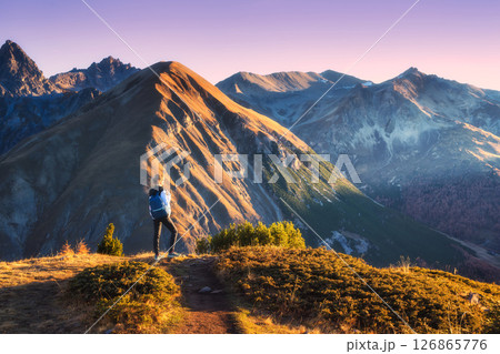 Young woman with backpack standing on grassy mountain trail 126865776