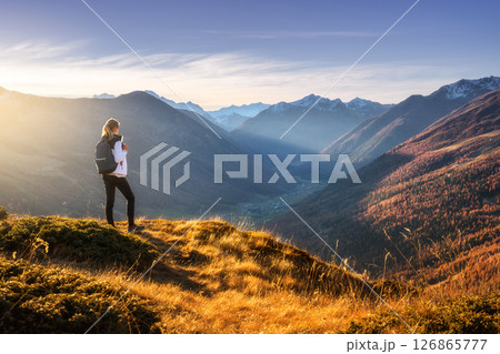 Young woman with backpack standing on grassy mountain ridge Young woman with backpack standing on grassy mountain ridge 126865777
