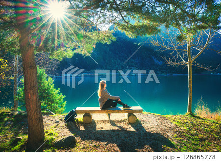 Young woman sitting on the bench under trees near lake at sunris 126865778