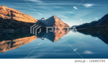 Sunset casts a serene glow on mountains mirrored in a alpine lake Sunset casts a serene glow on mountains mirrored in a alpine lake 126865785