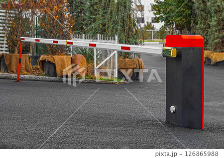 Parking system equipment in the form of a rack mounted in freshly laid black asphalt with a lifting white barrier with red discontinuous stripes and a support beam. Safety access and control tools Parking system equipment in the form of a rack mounted in freshly laid black asphalt with a lifting white barrier with red discontinuous stripes and a support beam. Safety access and control tools 126865988