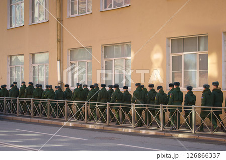a column of cadets of military forces walk along the fence and gates with the symbols of the armed forces 126866337