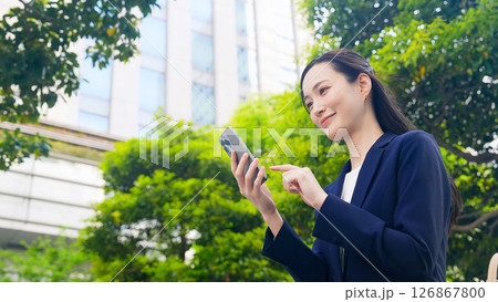 新緑の街でスマホを使う女性ビジネスパーソン 126867800