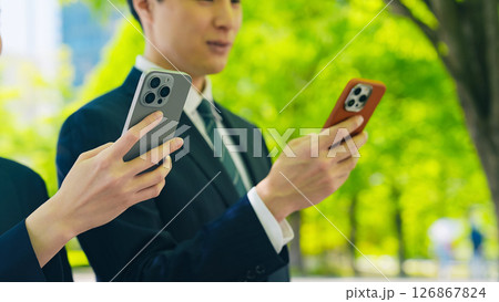 新緑の街でスマホを使う男女ビジネスパーソン 126867824