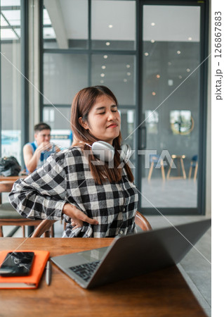 Young woman with headphones taking a break in a modern cafe, enjoying a moment of relaxation while working on her laptop. 126867883