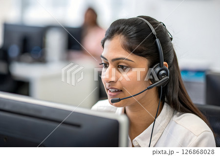Focused call center agent wearing headset in modern open office 126868028