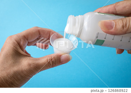 Pouring liquid medicine or antacid onto cup. 126868922