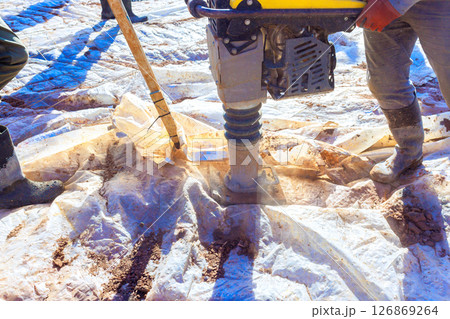 Construction workers use compactor to pack down soil on construction site under works day. Construction workers use compactor to pack down soil on construction site under works day. 126869264