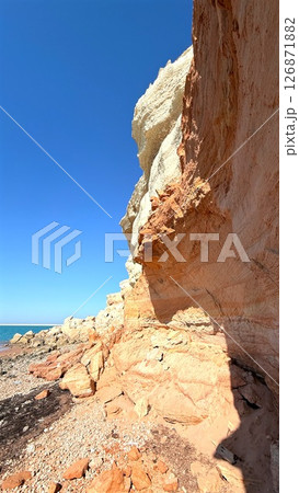 Colorful fossil rock formations rising on the seashore, creating dramatic contrast against clear blue sky, offering picturesque view of coastal geology Colorful fossil rock formations rising on the seashore, creating dramatic contrast against clear blue sky, offering picturesque view of coastal geology 126871882