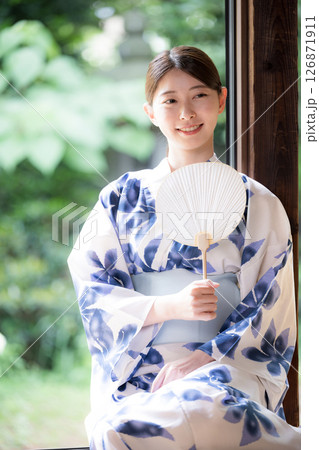 縁側に座る団扇を持った浴衣の女性のカメラ目線の全身縦 日本の夏イメージ 縁側に座る団扇を持った浴衣の女性のカメラ目線の全身縦 日本の夏イメージ 126871911